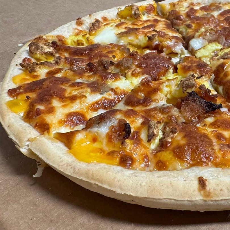 Close-up of a Joe's Pizza breakfast pizza with scrambled eggs, sausage, and melted cheese.