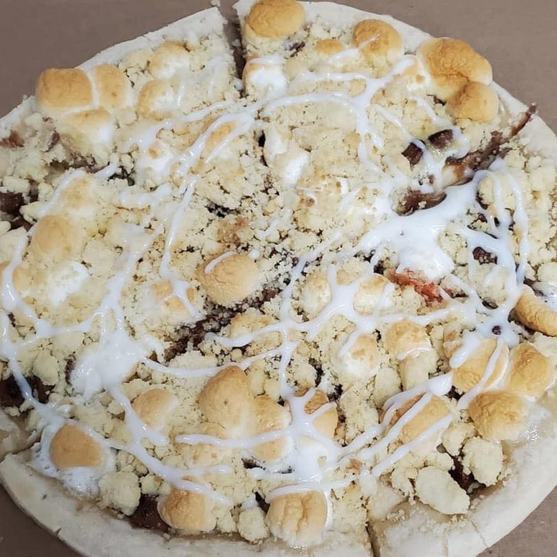 A dessert pizza from Joe's Pizza, topped with crumbled streusel, toasted marshmallows, and white icing.