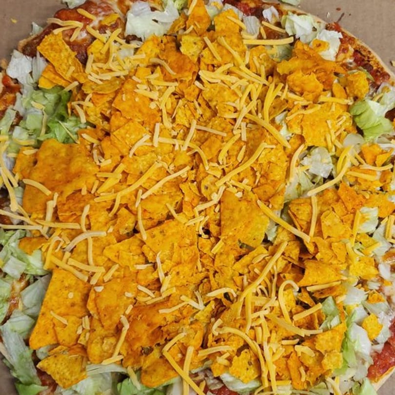 Joe's Pizza taco pizza topped with shredded lettuce, Doritos, and shredded cheese.