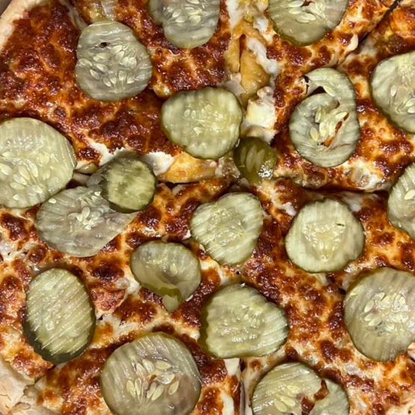 Close-up of a Joe's Pizza pie topped with melted cheese and numerous pickle slices.