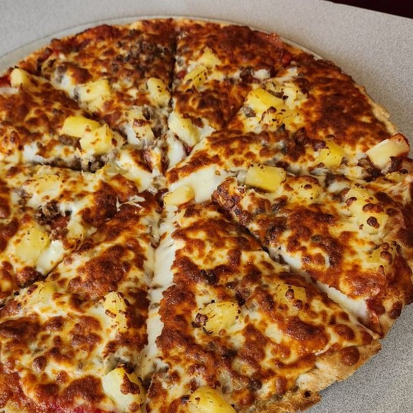 A Joe's Pizza pie, cut into slices, topped with melted cheese, ground meat, and pineapple.